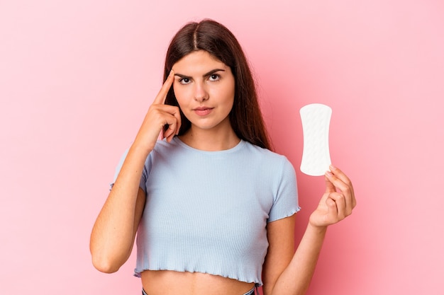 Jonge blanke vrouw met een kompres geïsoleerd op roze achtergrond wijzende tempel met vinger, denken, gericht op een taak.