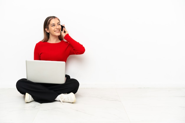 Jonge blanke vrouw met een laptop zittend op de vloer een gesprek te houden