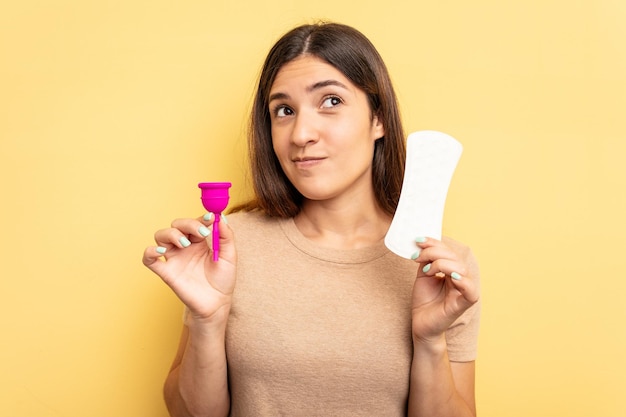 Jonge blanke vrouw met een menstruatiecup geïsoleerd op gele achtergrond