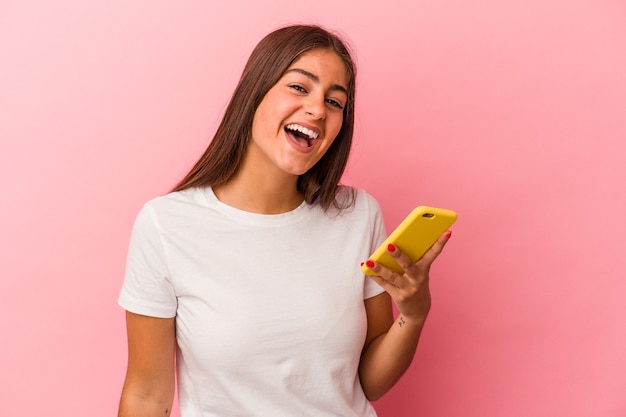 Jonge blanke vrouw met een mobiele telefoon geïsoleerd op roze achtergrond lachen en plezier maken.