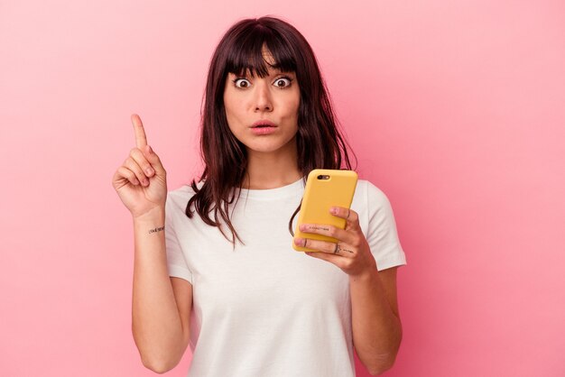 Jonge blanke vrouw met een mobiele telefoon geïsoleerd op roze muur met een geweldig idee