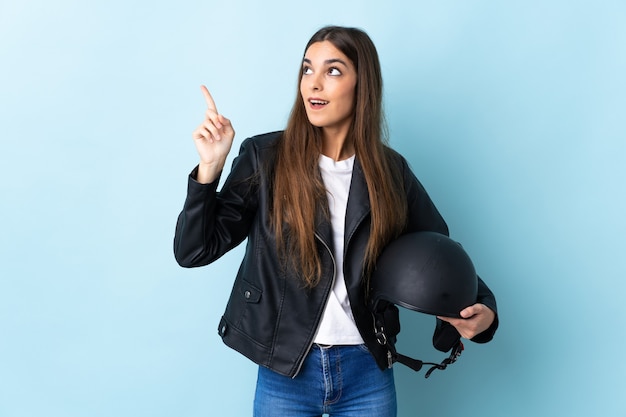 Jonge blanke vrouw met een motorhelm geïsoleerd op blauwe achtergrond met de bedoeling de oplossing te realiseren terwijl het opheffen van een vinger