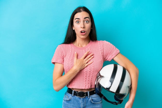 Jonge blanke vrouw met een motorhelm geïsoleerd op blauwe achtergrond verrast en geschokt terwijl ze naar rechts kijkt