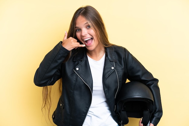 Jonge blanke vrouw met een motorhelm geïsoleerd op een gele achtergrond die een telefoongebaar maakt Bel me terug-teken