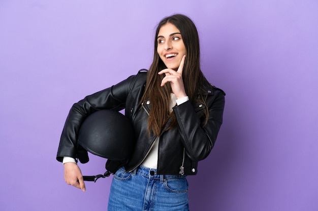 Jonge blanke vrouw met een motorhelm geïsoleerd op een paarse achtergrond die een idee denkt terwijl ze omhoog kijkt