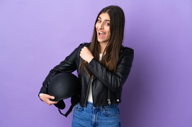 Jonge blanke vrouw met een motorhelm geïsoleerd op een paarse achtergrond die een overwinning viert