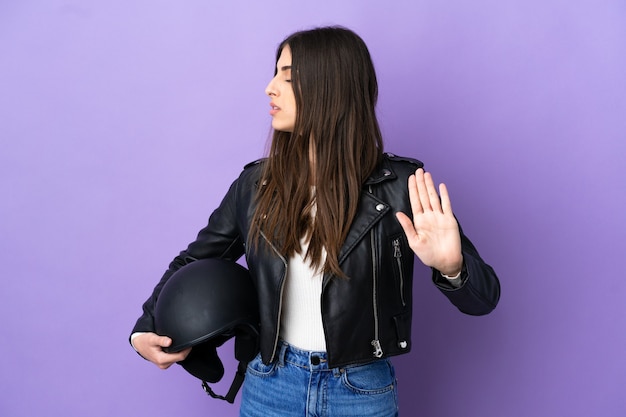 Jonge blanke vrouw met een motorhelm geïsoleerd op een paarse achtergrond die een stopgebaar maakt en teleurgesteld is?