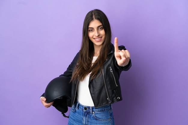 Jonge blanke vrouw met een motorhelm geïsoleerd op een paarse achtergrond die een vinger laat zien en optilt