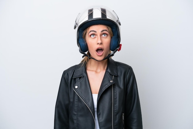 Jonge blanke vrouw met een motorhelm geïsoleerd op een witte achtergrond opzoeken en met verbaasde expressie