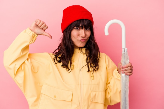 Jonge blanke vrouw met een paraplu geïsoleerd op roze achtergrond voelt zich trots en zelfverzekerd, voorbeeld om te volgen.