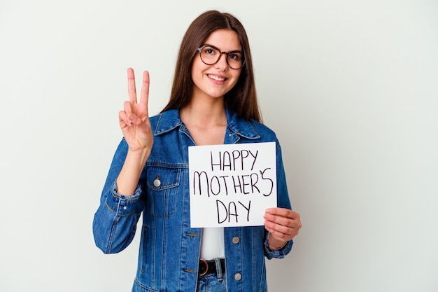 Jonge blanke vrouw met een plakkaat gemaakt met liefde geïsoleerd op een witte muur kijkt opzij glimlachend, vrolijk en aangenaam.