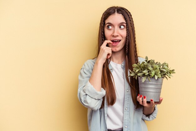 Jonge blanke vrouw met een plant geïsoleerd op een gele achtergrond ontspannen denkend aan iets dat naar een kopieerruimte kijkt