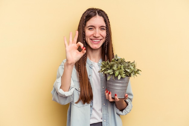 Jonge blanke vrouw met een plant geïsoleerd op een gele achtergrond, vrolijk en zelfverzekerd met een goed gebaar