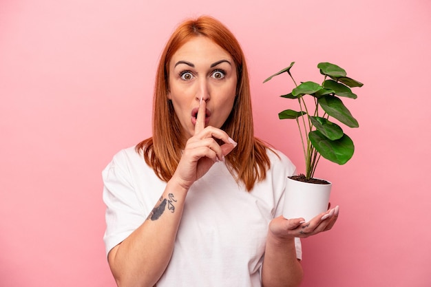 Jonge blanke vrouw met een plant geïsoleerd op roze achtergrond Jonge blanke vrouw met een plant geïsoleerd op roze achtergrond een geheim bewaren of om stilte vragen.