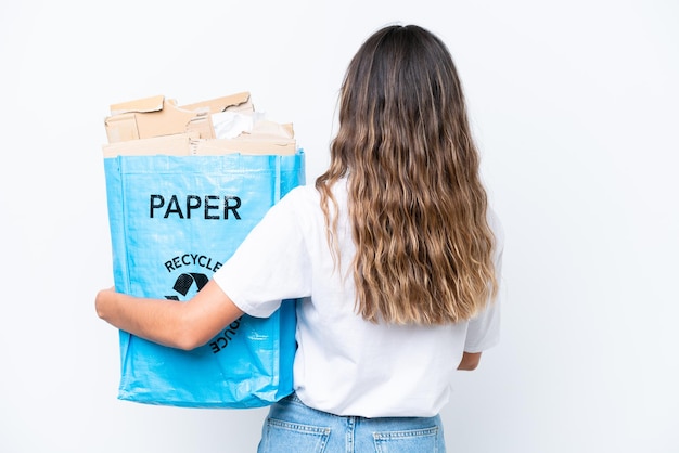 Jonge blanke vrouw met een recyclingzak vol papier om te recyclen geïsoleerd op een witte achtergrond in de achterste positie