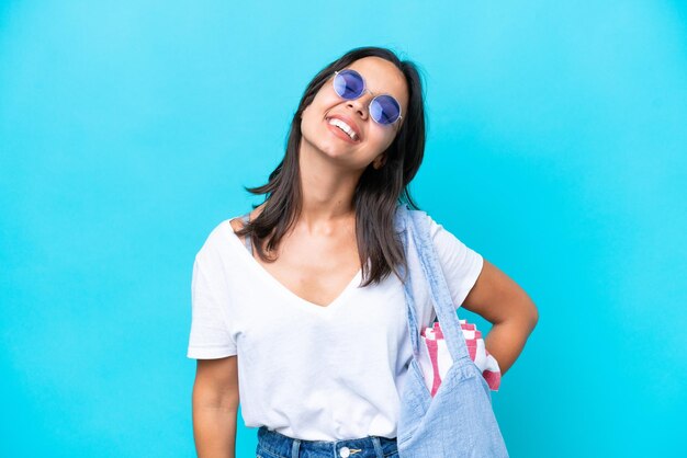 Jonge blanke vrouw met een strandtas geïsoleerd op blauwe achtergrond lachen