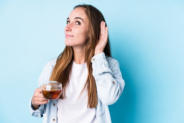 Jonge blanke vrouw met een thee geïsoleerd proberen te luisteren van een roddel.