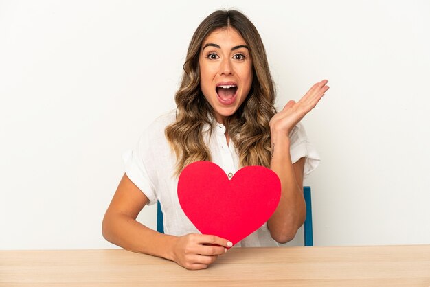 Jonge blanke vrouw met een Valentijnsdag hart geïsoleerd verrast en geschokt.