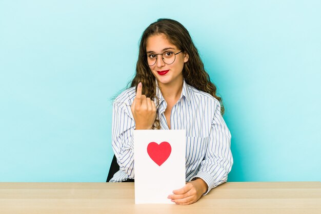 Jonge blanke vrouw met een Valentijnsdag kaart geïsoleerd met de vinger naar je wijzend alsof ze dichterbij komen.