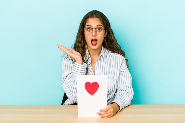 Jonge blanke vrouw met een Valentijnsdag kaart geïsoleerd verrast en geschokt.