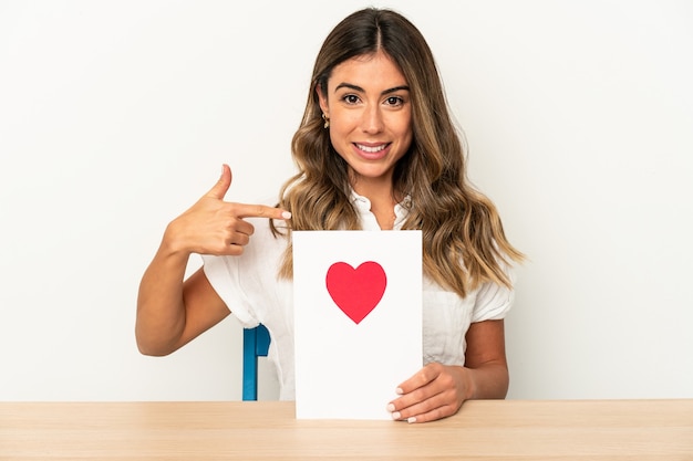 Jonge blanke vrouw met een valentijnsdag kaart geïsoleerde persoon met de hand wijzend naar een shirt kopie ruimte, trots en zelfverzekerd