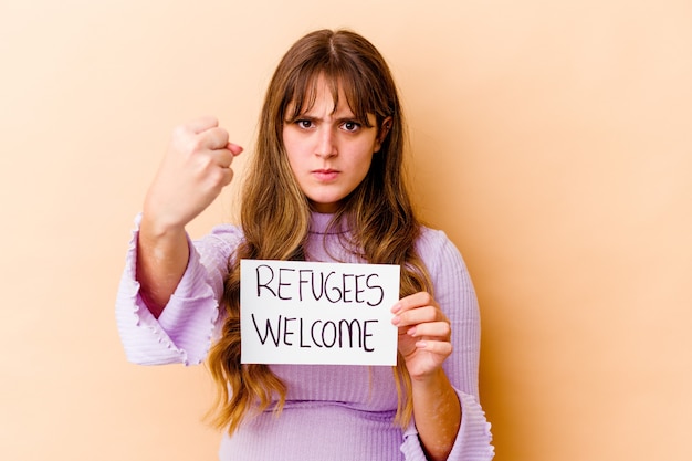 Foto jonge blanke vrouw met een vluchtelingen welkom bordje geïsoleerd met vuist, agressieve gezichtsuitdrukking.