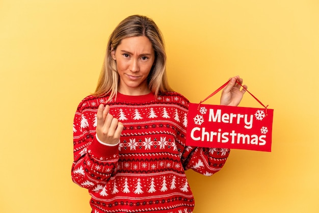 Jonge blanke vrouw met een vrolijk kerstfeestje geïsoleerd op een gele achtergrond die met de vinger naar je wijst alsof uitnodigend dichterbij komt.
