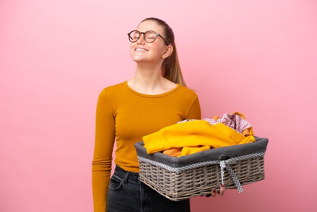 Jonge blanke vrouw met een wasmand geïsoleerd op roze achtergrond lachen