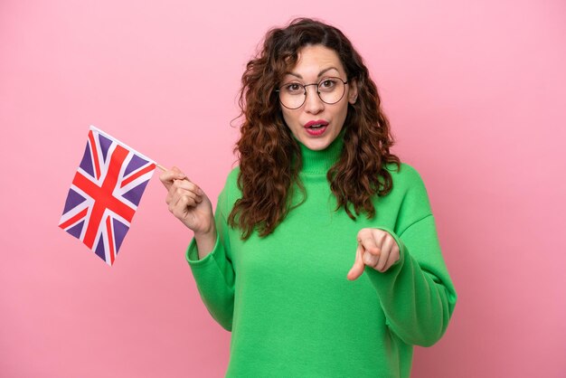 Jonge blanke vrouw met Engelse vlag geïsoleerd op roze achtergrond verrast en wijzend naar voren