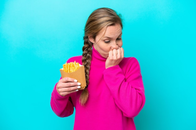 Jonge blanke vrouw met gefrituurde chips geïsoleerd op een blauwe achtergrond met twijfels