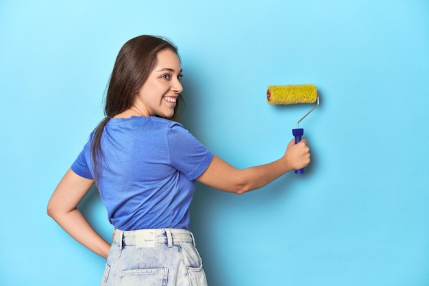 Jonge blanke vrouw met gele verfroller op blauwe studio