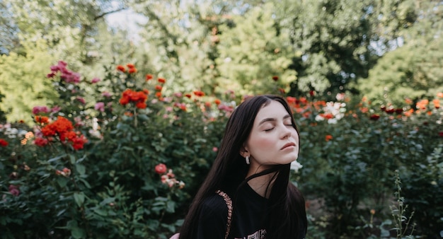 Jonge blanke vrouw met gesloten ogen genieten van lenteweer op tuin met bloeiende rozen.