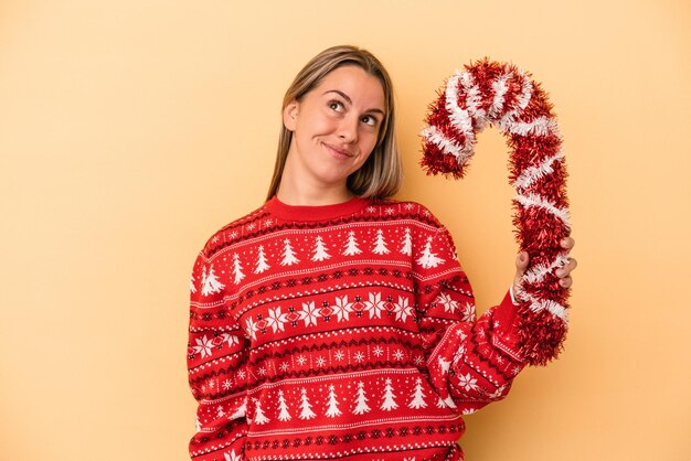 Jonge blanke vrouw met grote kerststok geïsoleerd op gele achtergrond dromen van het bereiken van doelen en doeleinden