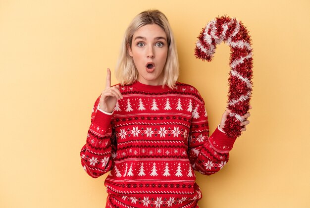 Jonge blanke vrouw met grote kerststok geïsoleerd op gele achtergrond met een idee, inspiratie concept.