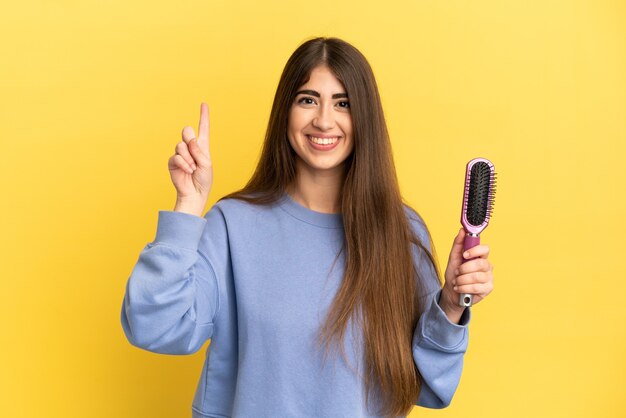 Jonge blanke vrouw met haarborstel geïsoleerd op een blauwe achtergrond die een geweldig idee benadrukt