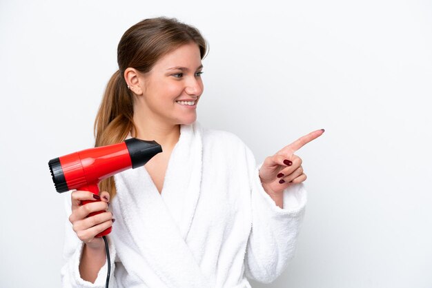 Jonge blanke vrouw met haardroger geïsoleerd op een witte achtergrond, wijzend naar de zijkant om een product te presenteren