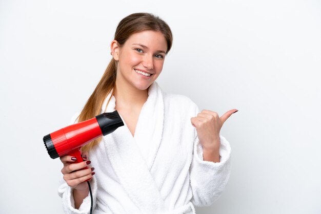 Jonge blanke vrouw met haardroger geïsoleerd op een witte achtergrond, wijzend naar de zijkant om een product te presenteren