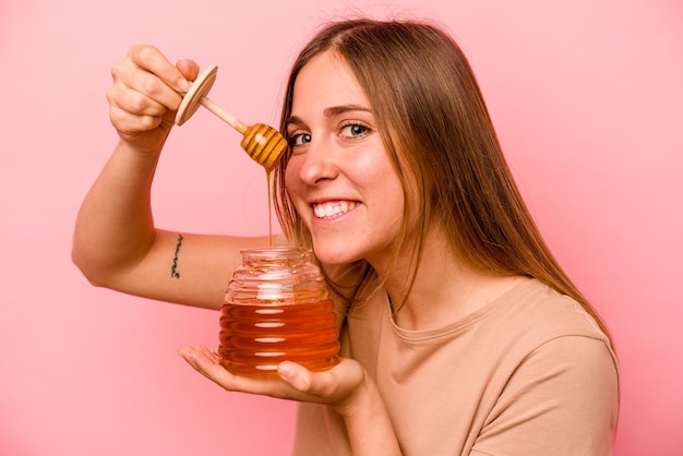 Jonge blanke vrouw met honing geïsoleerd op roze background