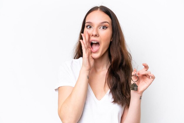 Jonge blanke vrouw met huissleutels geïsoleerd op witte achtergrond schreeuwend met haar mond wijd open
