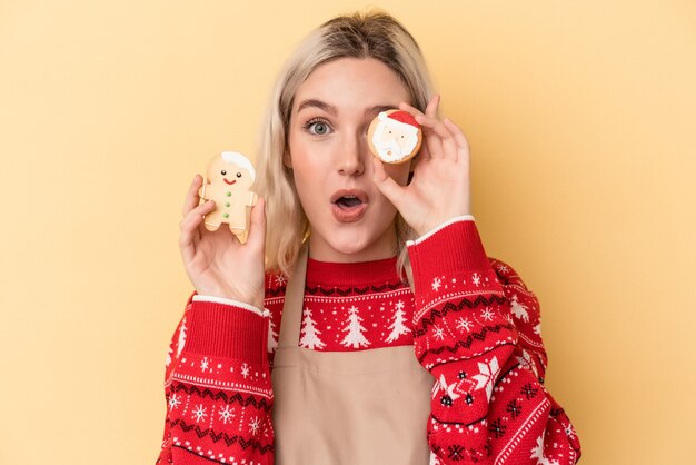 Jonge blanke vrouw met kerstkoekjes geïsoleerd op gele achtergrond