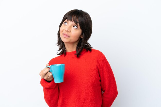 Jonge blanke vrouw met kopje koffie geïsoleerd op een witte achtergrond en denkt aan een idee terwijl ze omhoog kijkt