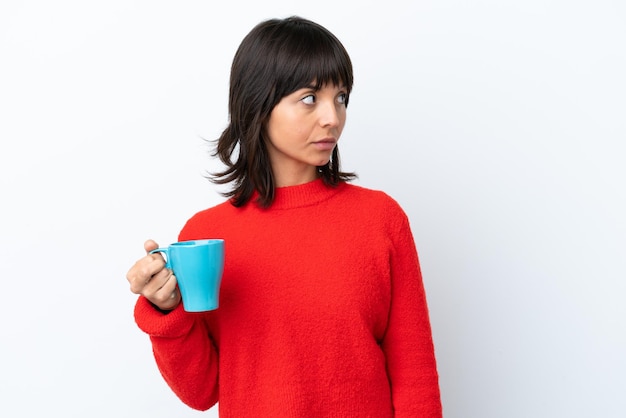 Jonge blanke vrouw met kopje koffie geïsoleerd op een witte achtergrond op zoek naar de zijkant