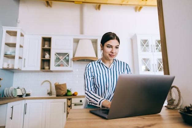 Jonge blanke vrouw met lap top computer, zittend op de keuken thuis.