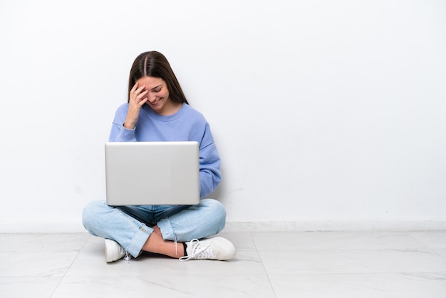 Jonge blanke vrouw met laptop zittend op de vloer geïsoleerd op een witte achtergrond lachen