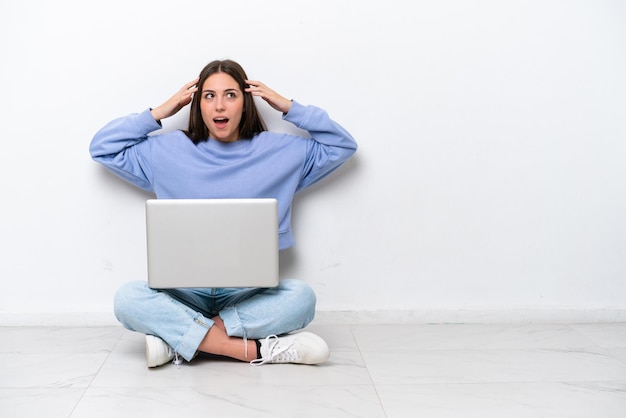 Jonge blanke vrouw met laptop zittend op de vloer geïsoleerd op een witte achtergrond met verrassing expression