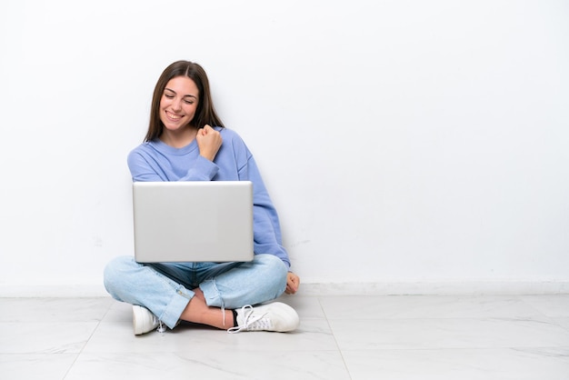 Jonge blanke vrouw met laptop zittend op de vloer geïsoleerd op een witte achtergrond vieren een overwinning