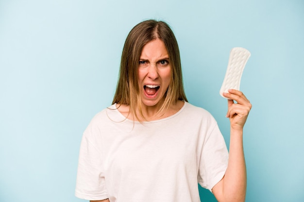 Jonge blanke vrouw met maandverband geïsoleerd op blauwe achtergrond schreeuwend erg boos en agressief