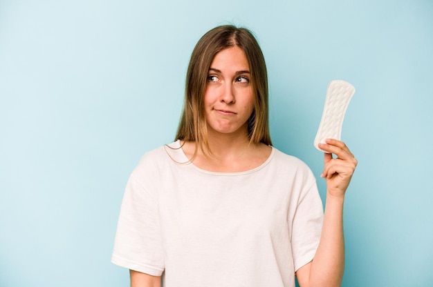 Jonge blanke vrouw met maandverband geïsoleerd op een blauwe achtergrond verward voelt zich twijfelachtig en onzeker