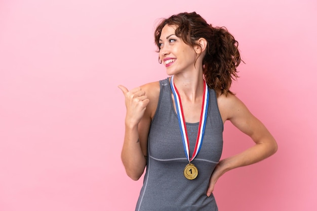 Jonge blanke vrouw met medailles geïsoleerd op een roze achtergrond die naar de zijkant wijst om een product te presenteren