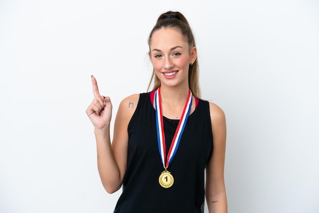 Jonge blanke vrouw met medailles geïsoleerd op een witte achtergrond die een vinger toont en opheft in teken van de beste